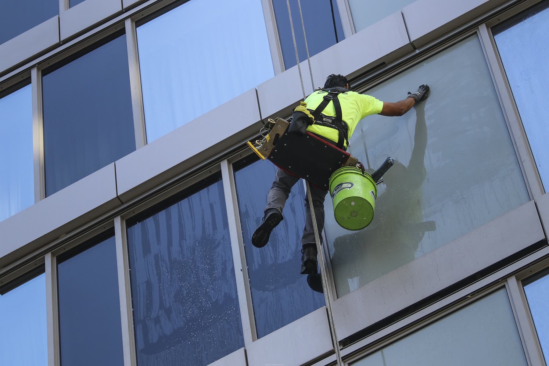 Fassadenreiniger in Warnschutzkleidung wischt am Seil eine Glasfassade